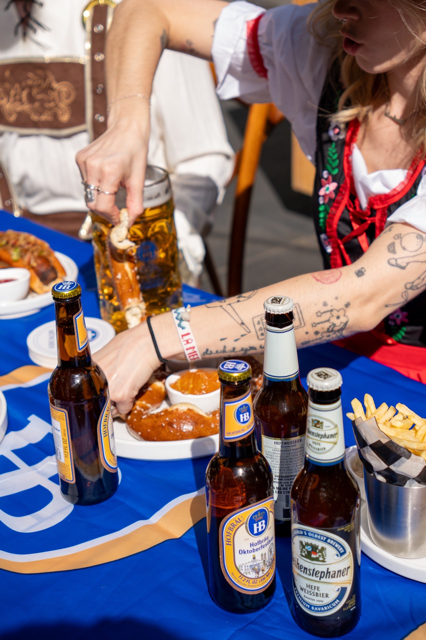 A rooftop table set with Hofbräu and Weihenstephaner Oktoberfest bottles, a soft pretzel and bratwurst
