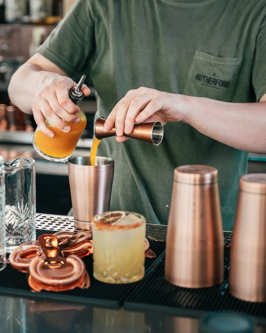 A bartender pouring a fresh juice into a copper shaker among the bar's cocktail tools