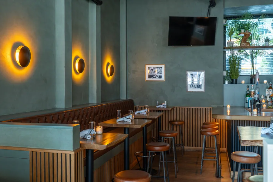 A leather booth at The Rutherford beneath a wall-mounted screen and framed vintage sports photos