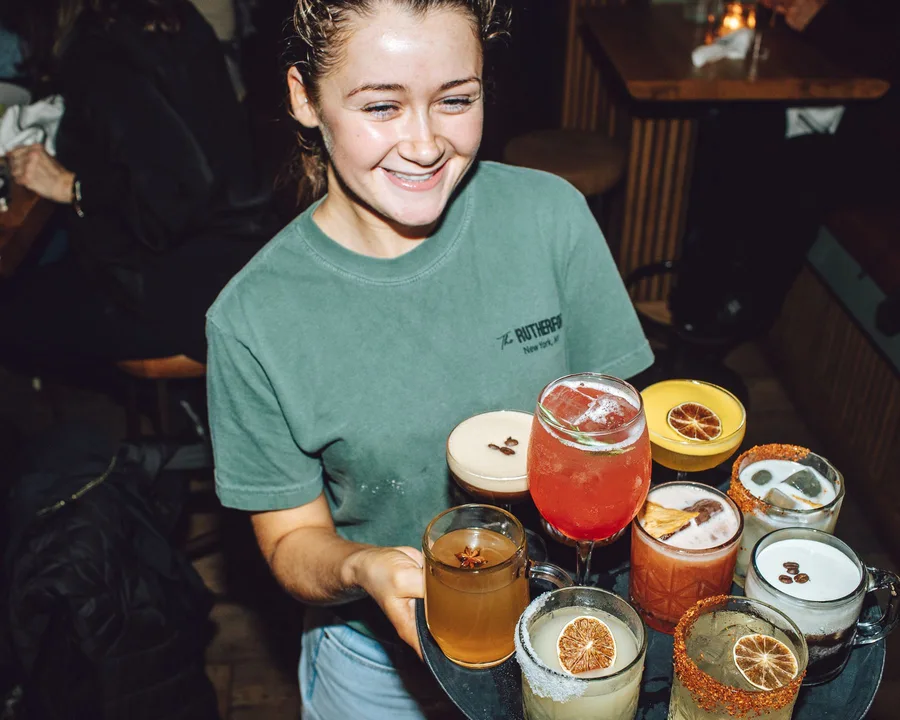 A server carrying a full tray of cocktails across the room